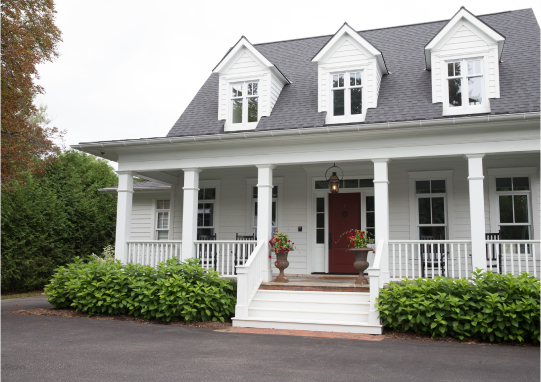 White house with a covered front porch, three dormer windows, and a red front door