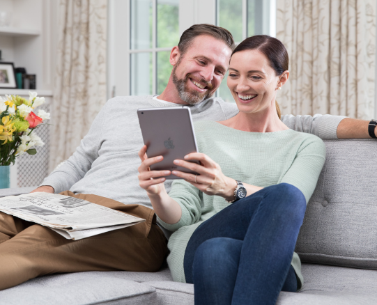 Smiling couple relaxing on a sofa and looking at a tablet in a bright living room