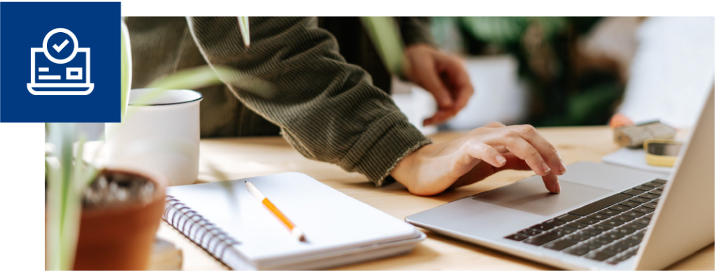 A hand uses a silver laptop to book home inspections with Pillar To Post's Online Booking system. In the top left hand corner in a blue box is an icon with a laptop and a checkmark in a circle.
