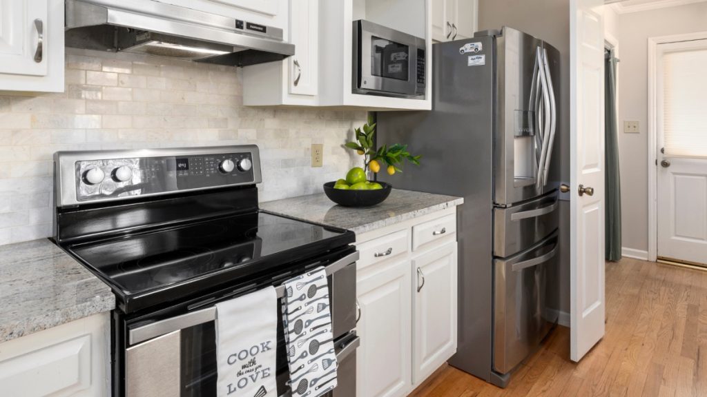 Bright kitchen with stainless steel range and French-door refrigerator, white cabinets, and stone countertop