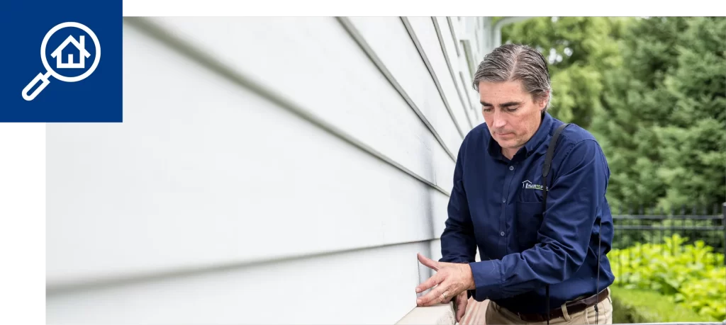 Home inspector examining the exterior siding of a house outdoors.